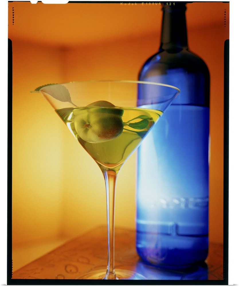 Big vertical photograph of fruit martini in a glass, sitting on a counter in front of a blue bottle.