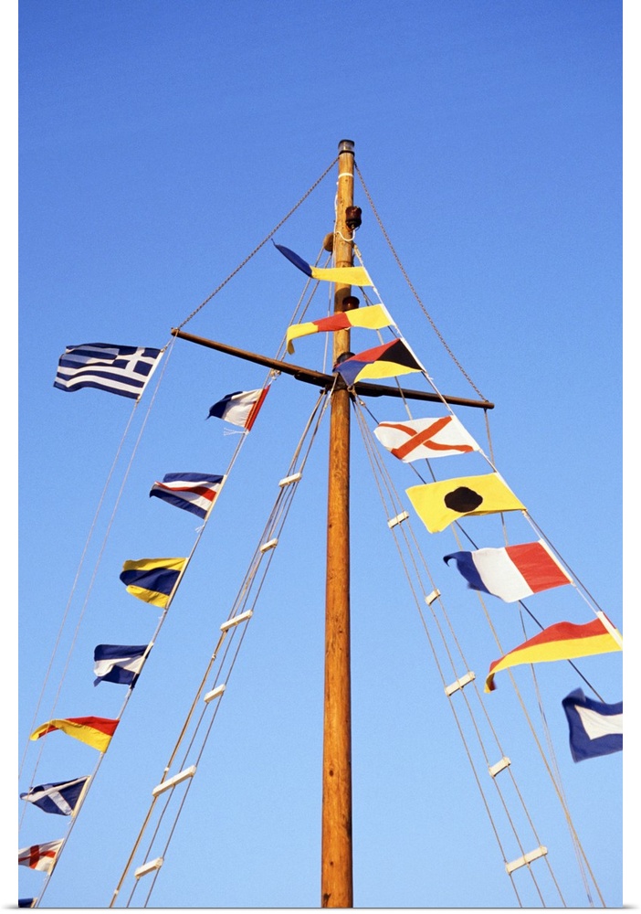 Multiple flags on the mast of a sailboat against a blue sky.