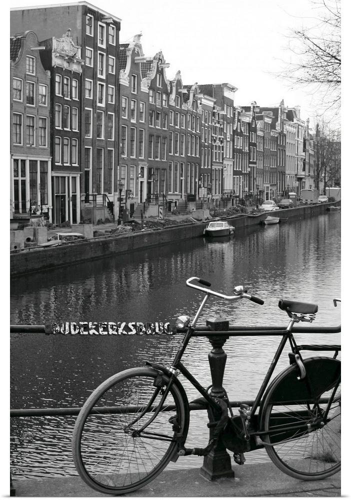 Vertical canvas photo art of a bike leaning against a railing in front of a river running through an European city.