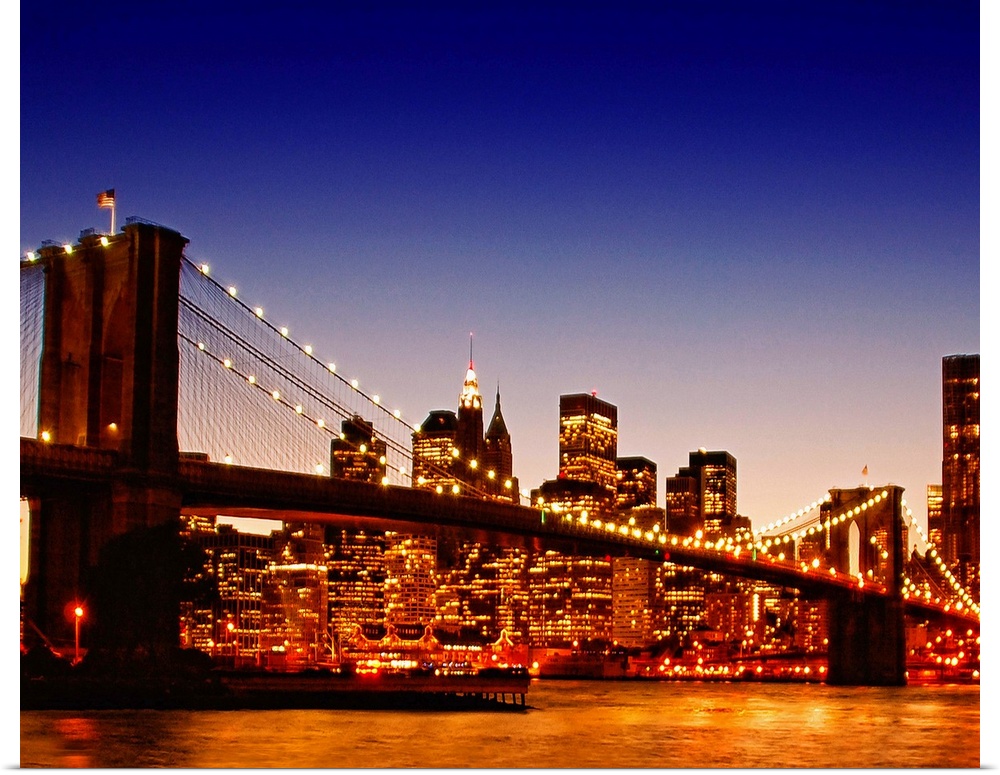 Large photograph of the Brooklyn bridge with a sun kissed river below at dusk with NYC lit up in the background.