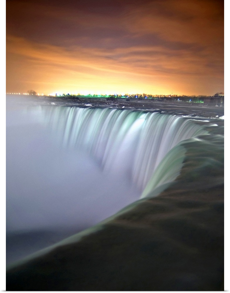 This vertical photograph captures the growing light in the eastern horizon and the massive cascades of the waterfall from ...