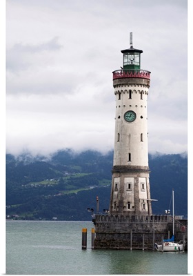 old lighthouse on a pier of a lake with cloud covered mountains in the background