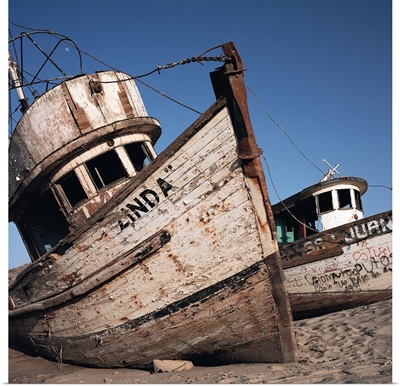 old neglected boats sit beached on sand under a blue sky