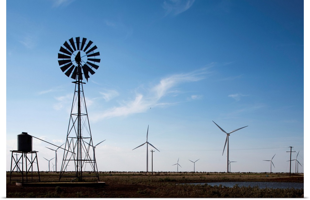 USA, Texas, Vega, Old ranch windmill and water pump beneath array of wind power generating turbines at Wildorado Wind Farm...
