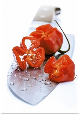 Partly sliced habanero chillies on knife, close-up