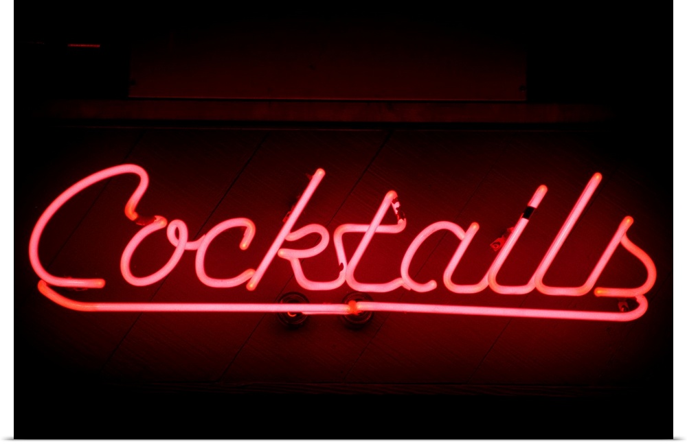 An illuminated pink sign with the work cocktails sits on a dark wall.