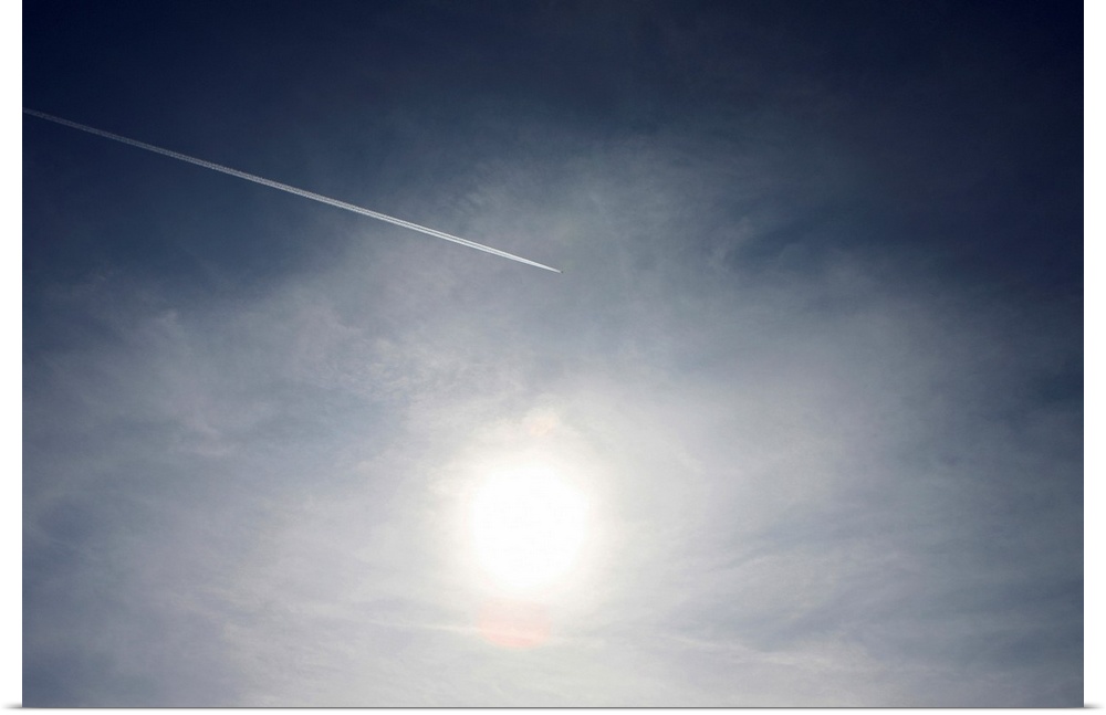 Plane and Vapor trail flying above sun.
