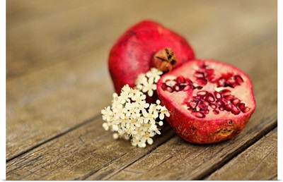 Pomegranate fruit with cluster of tiny white flowers on rustic wooden tabletop.