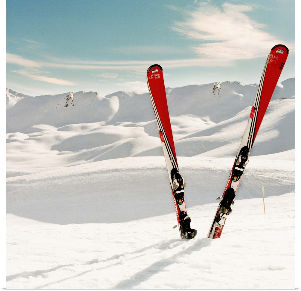 Red pair of ski standing in snow.Mountains in background