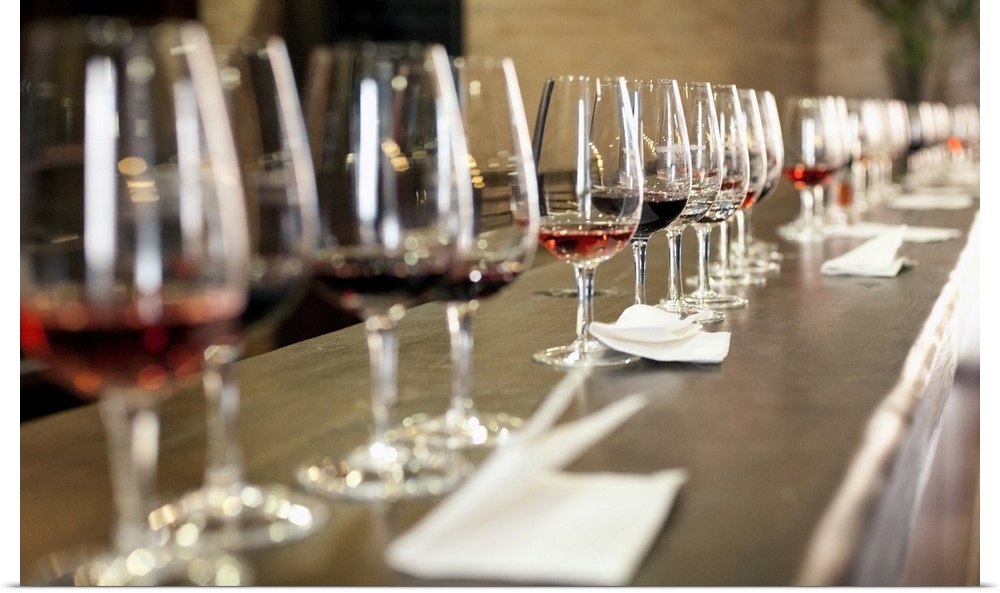 A long row of wine glasses set up so a large group of people can taste wines
