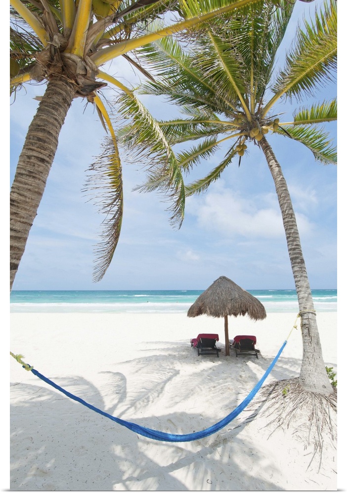 Tropical summer beach resort with chaise lounge beach chairs, hammock and palm trees in Tulum, Mexico.