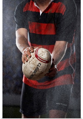 Rugby player holding ball in rain, mid section