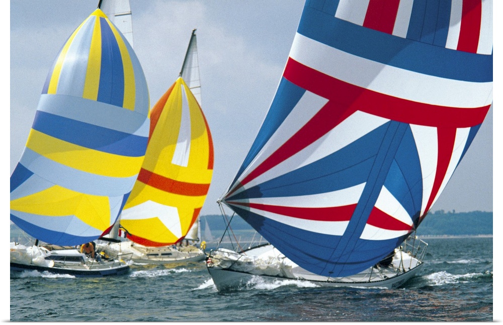 Boldly colored sails from three yachts in the midst of a race lean against the wind as the boats take a sharp turn.
