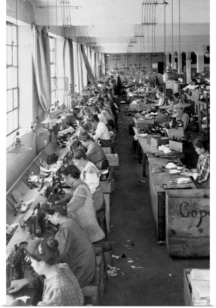 Shoe factory workers sewing on long tables.