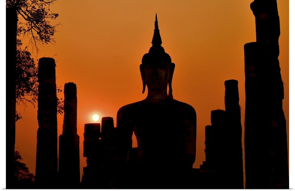 Silhouette of ancient Buddha statue sitting in middle of ruined temple (illustrated by remaining columns) in Sukhothai His...
