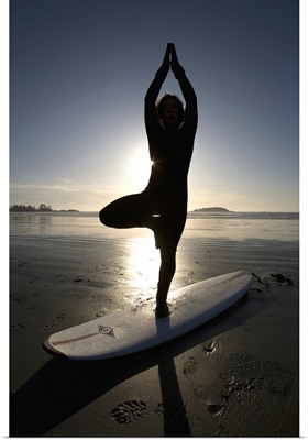 silhouette of female surfer doing yoga tree pose