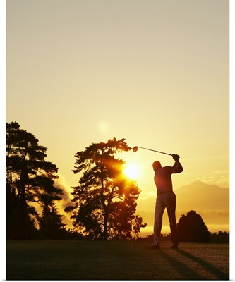 Silhouette of golfer swinging club on golf course at sunset
