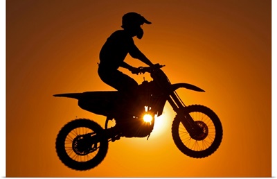 Silhouette of motocross race in mid air at sunset.