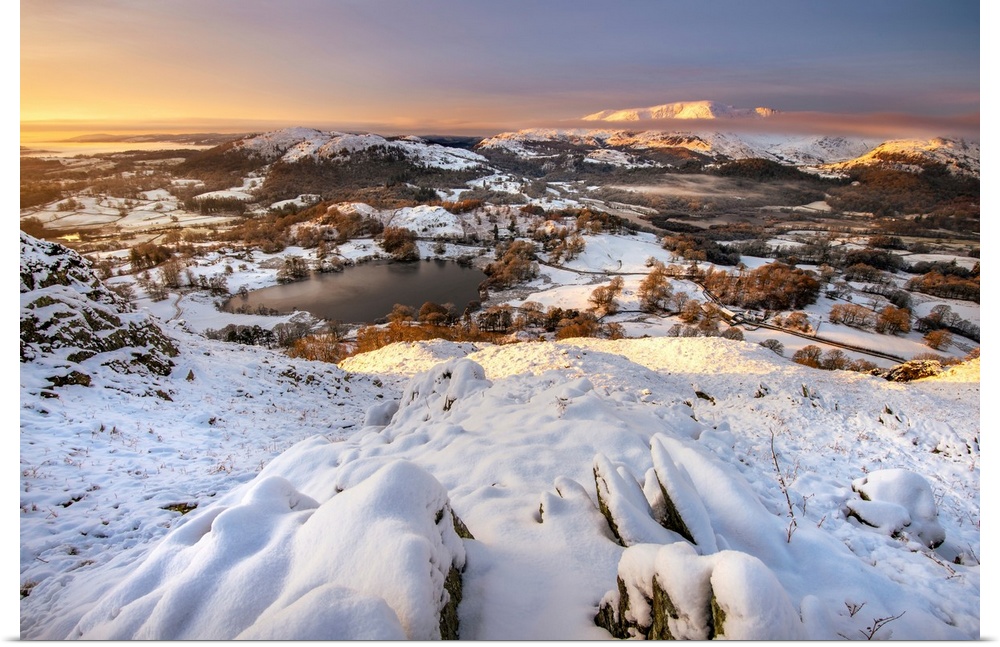 View from Loughrigg Fell on a winter morning with golden light bathing the snow covered landscape in Lake District, UK.