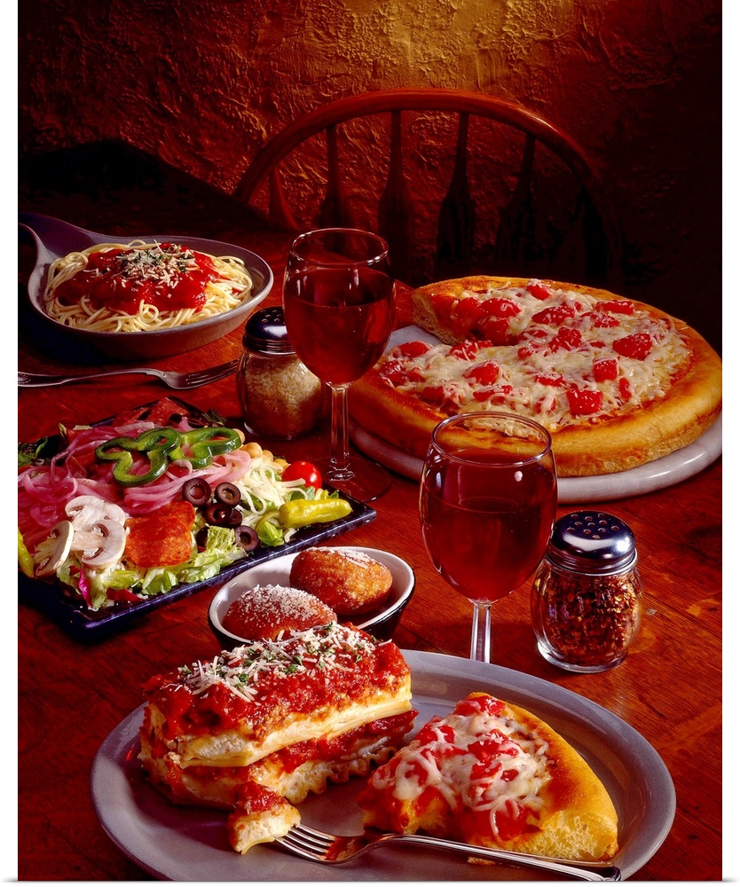 Photograph taken of a table covered with plates of Italian food that includes pasta, pizza and antipasto.