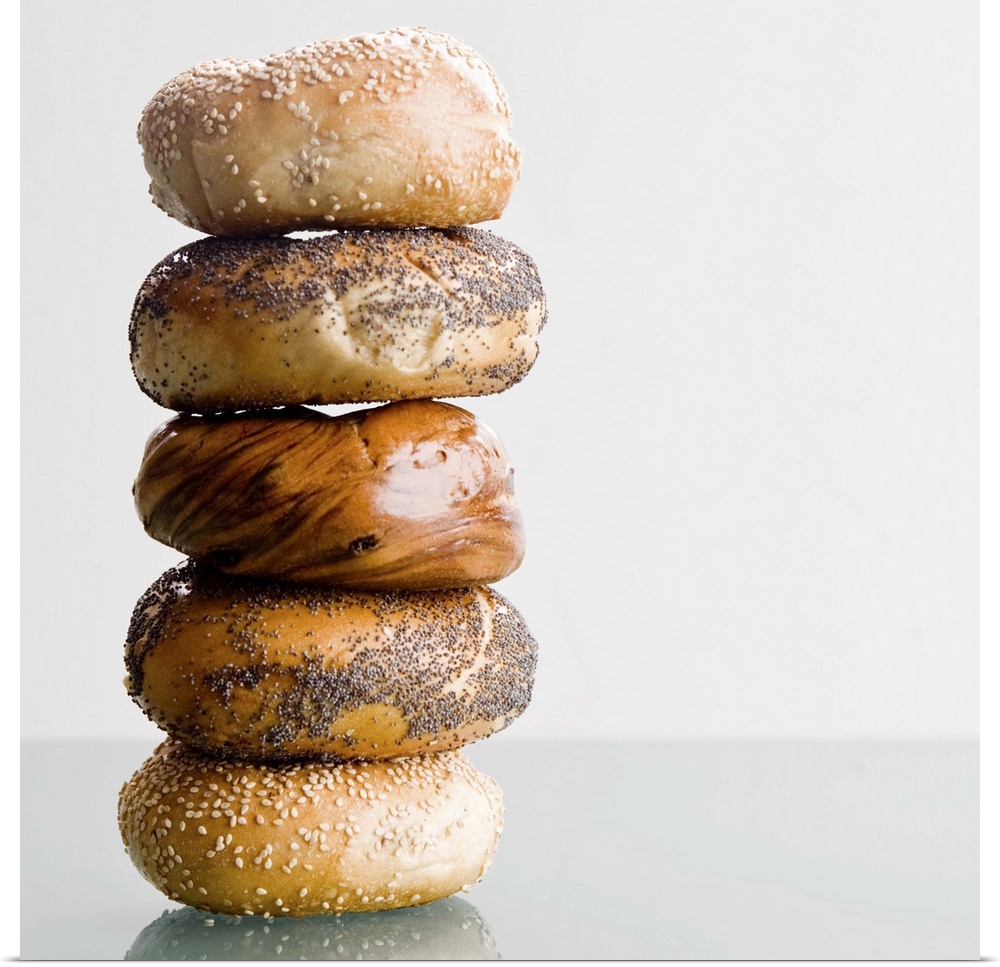 Different types of bagels are stacked high and photographed on a glass surface.
