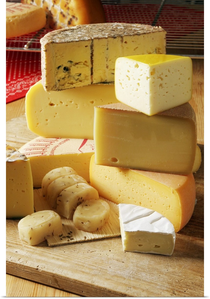 Big, vertical photograph of stacks of assorted light yellow and white cheeses, sitting on a wooden cutting board.