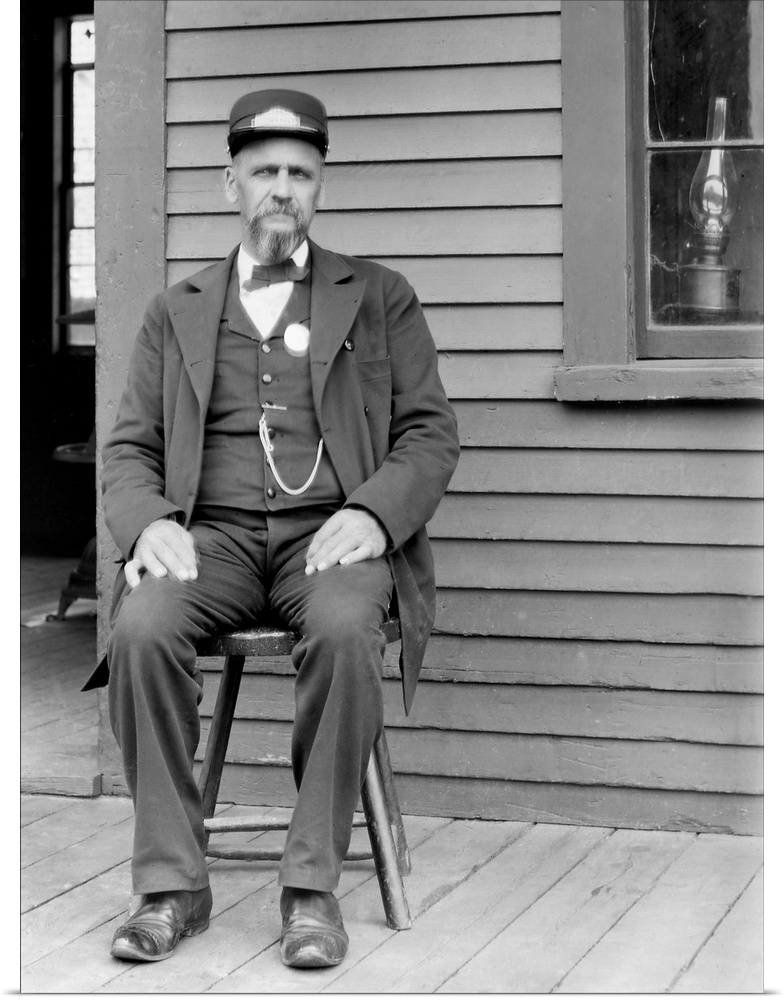 A Massachusetts train station worker sits on the platform next to a window with a lantern.