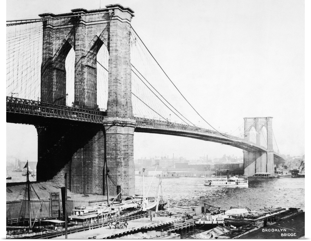 View of the Brooklyn Bridge showing docks and boat passing underneath.