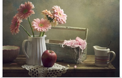 Still life with pink gerberas and red apple on table.