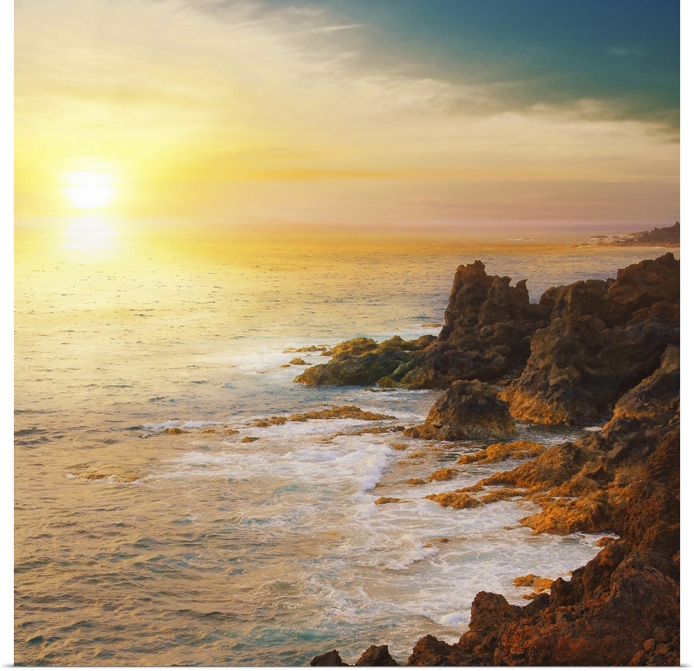 The sun is about to set below the horizon and a photograph is taken overlooking the ocean from a rocky coastline.