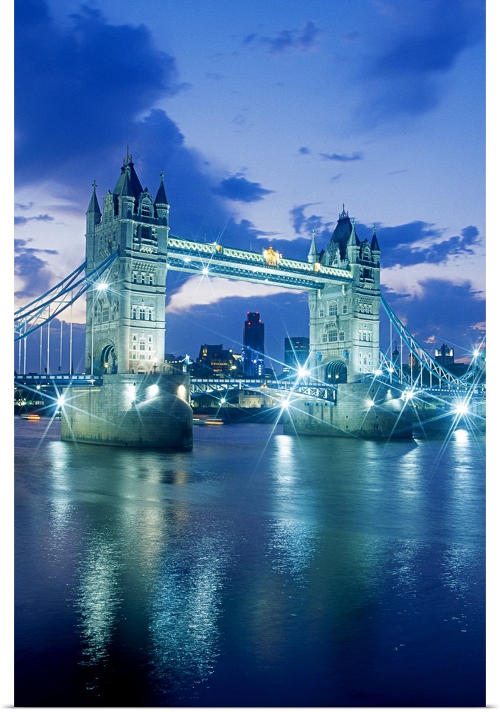 Vertical photograph on a large wall hanging of the Tower Bridge, lit up at night, the London skyline in the background, in...