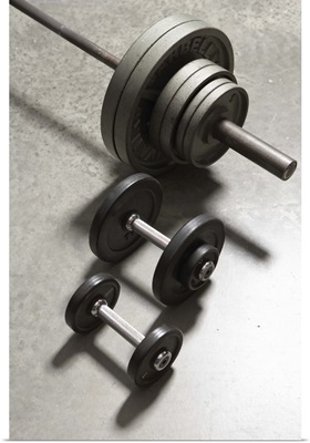 Two dumbbells and barbell side by side on concrete floor
