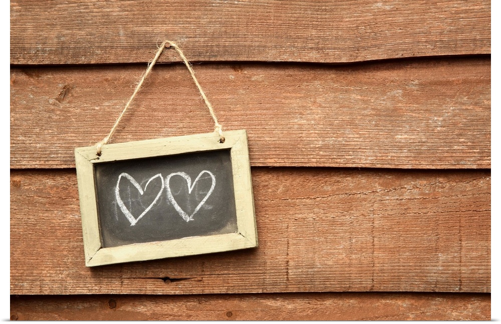 Two hearts drawn on small blackboard on garden fence