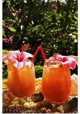Two tropical drinks garnished with flowers in an outdoor setting.