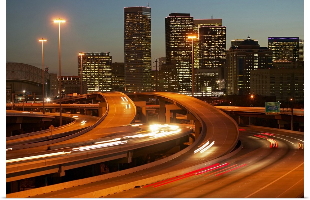 Photograph of the Houston skyline taken at night with the buildings lit up and cars lights streaking by on the highway.
