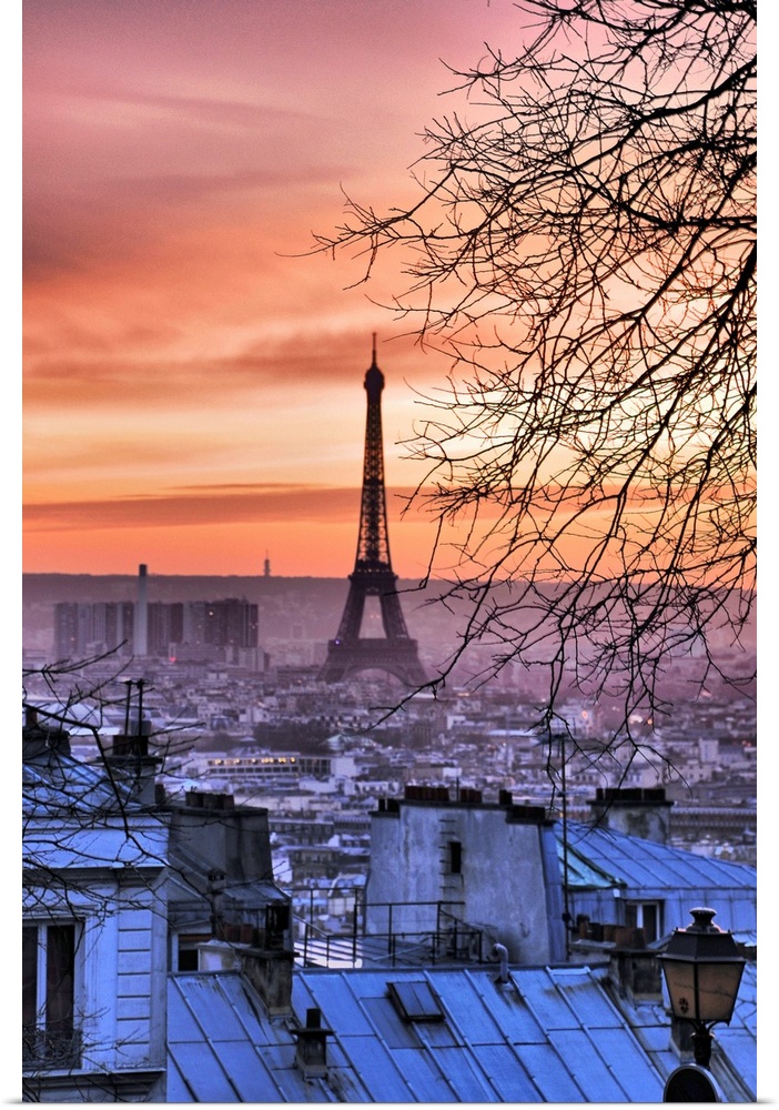 Photograph taken of the Eiffel Tower from a distance with a view of the city surrounding it. The sun is setting out of view.