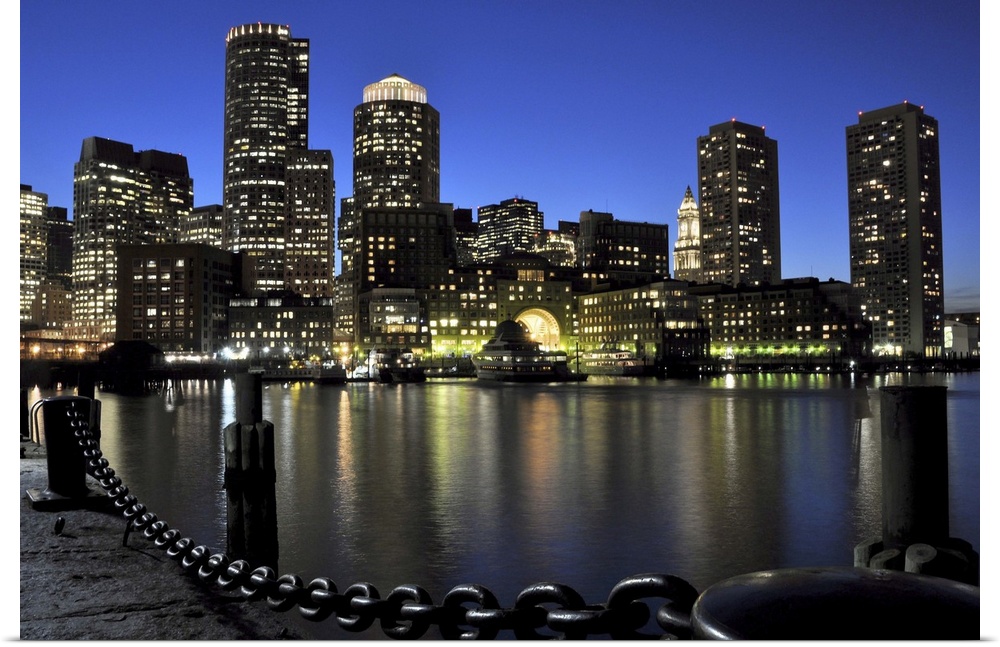Downtown Boston and Financial District skyline lit up against a deep blue, late twilight sky, with lights reflected in Bos...