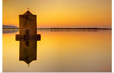 Windmill at sunset in middle of water and reflection in water.