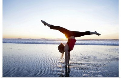 Woman doing a hand-stand on the beach at sunset
