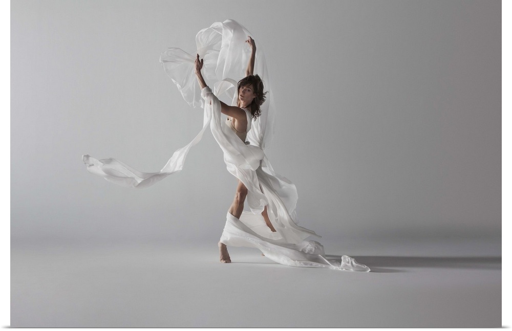 woman standing with white silk draped around her as fabric blows up and around her in wind.