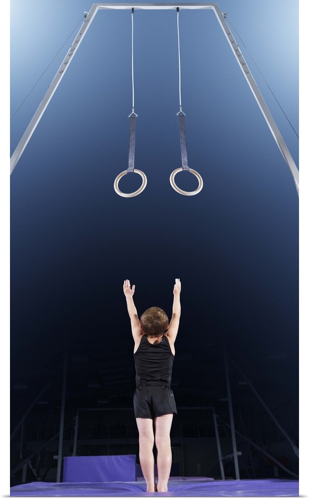 Young male gymnast reaching up to rings