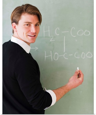 Young teacher writing equation on blackboard