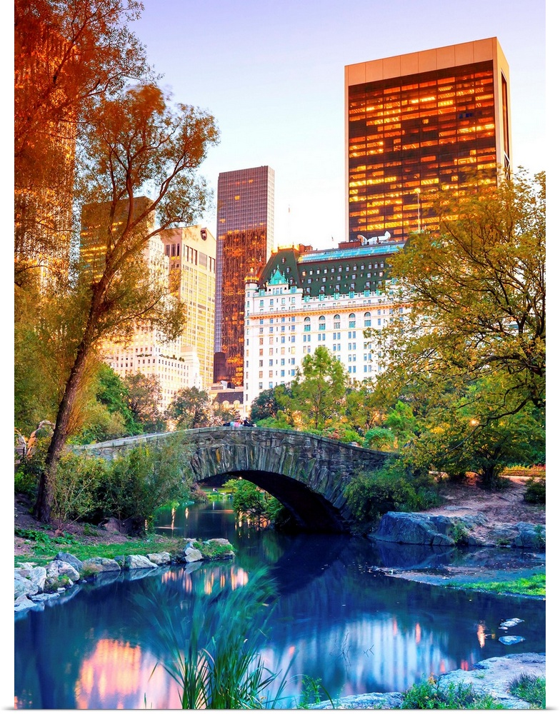 Vividly colored photograph of a bridge over a stream in Central Park, with skyscrapers in the distance.
