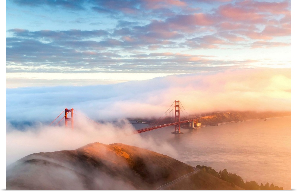 Aerial view of the Golden Gate Bridge surrounded by fog with the sunset coming in from the right.