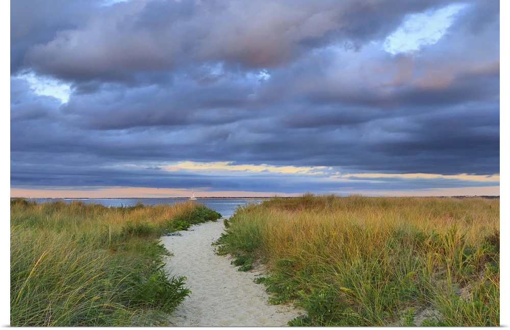 A photograph of a sandy pathway leading to an idyllic beach, with dark puffy clouds overhead.