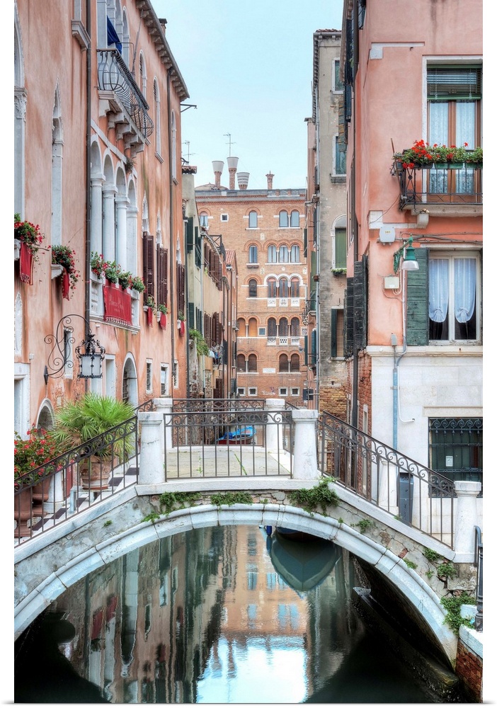 A vertical scene of a walking bridge over a canal with the city reflecting in the water in Venice, Italy.