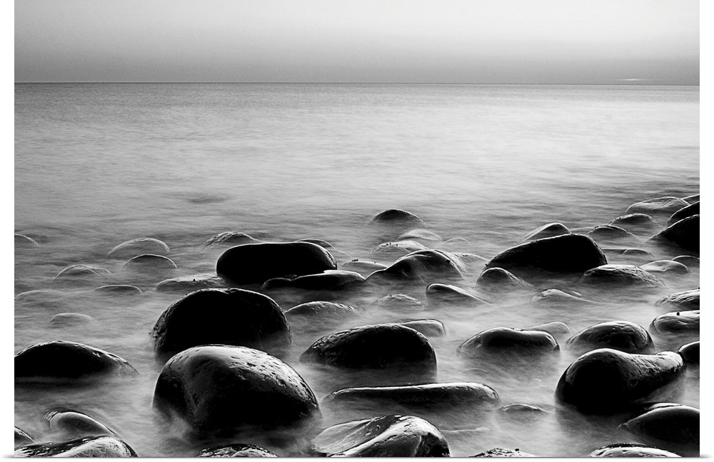 Black and white photograph of layers of smooth rocks covered by water.