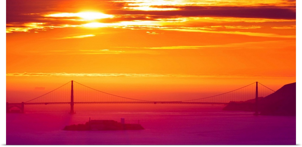 A photograph of a vibrant sky at sunrise, with a bridge in hazy, misty morning light.