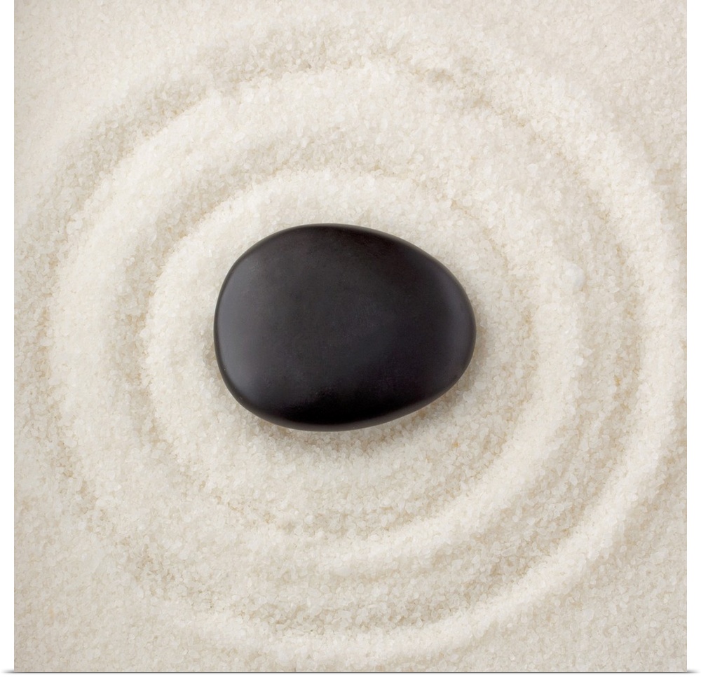 A smooth black rock in the middle of multiple rings in the sand.