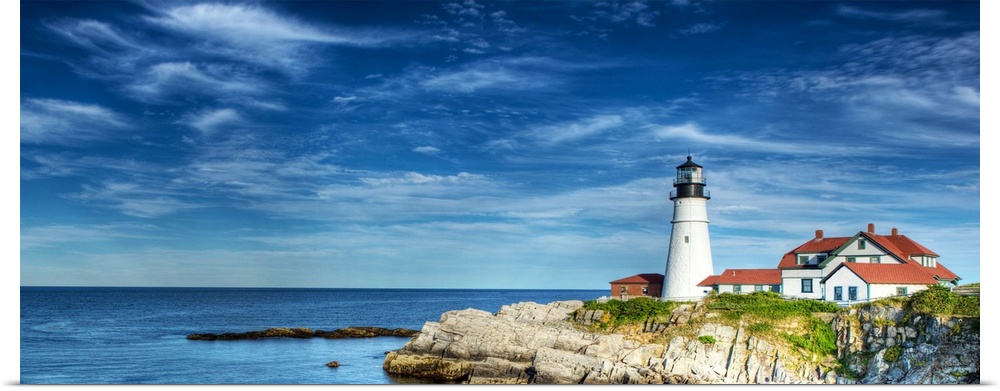Photograph of a lighthouse on the rocky shore against a blue sky.
